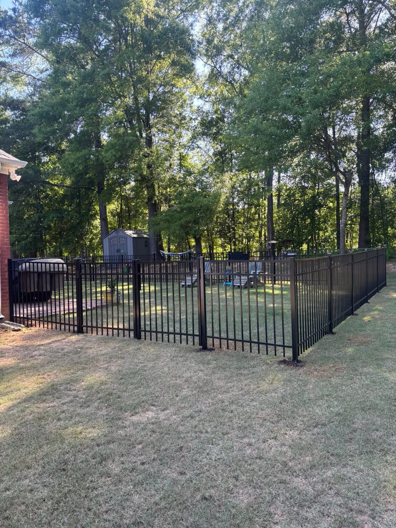 Black ornamental iron fence enclosing wooded backyard